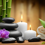 zen scene w bamboo, black rocks, purple orchid, white candles and a folded white towel