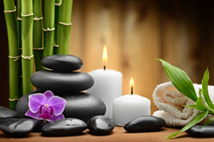 zen picture of green bamboo stalks, black stones, purple orchid, white candles and a white folded towel - spa like