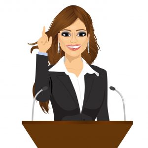 female speaker standing behind a podium with microphones. Speaker
