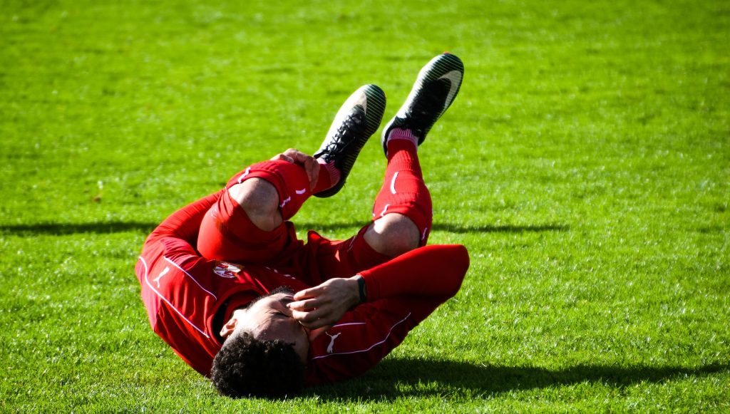 Athlete rolling on the grass - in pain because of leg cramps. Image by Shauking